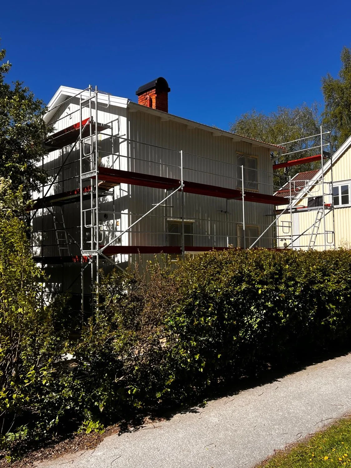 Fasadrenovering med byggställning på vitt trähus i Stockholm